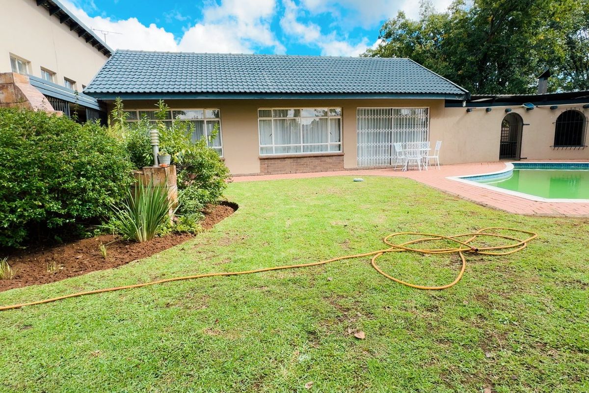 Rear garden view featuring a swimming pool, brick paved patio area, and established landscaping with a tiled roof dwelling.