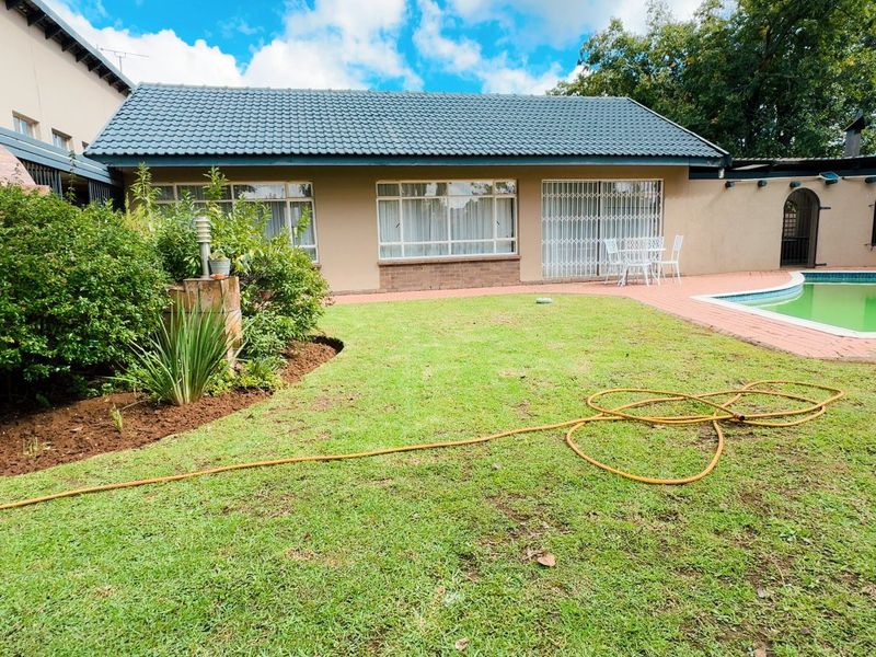 Rear garden view featuring a swimming pool, brick paved patio area, and established landscaping with a tiled roof dwelling.