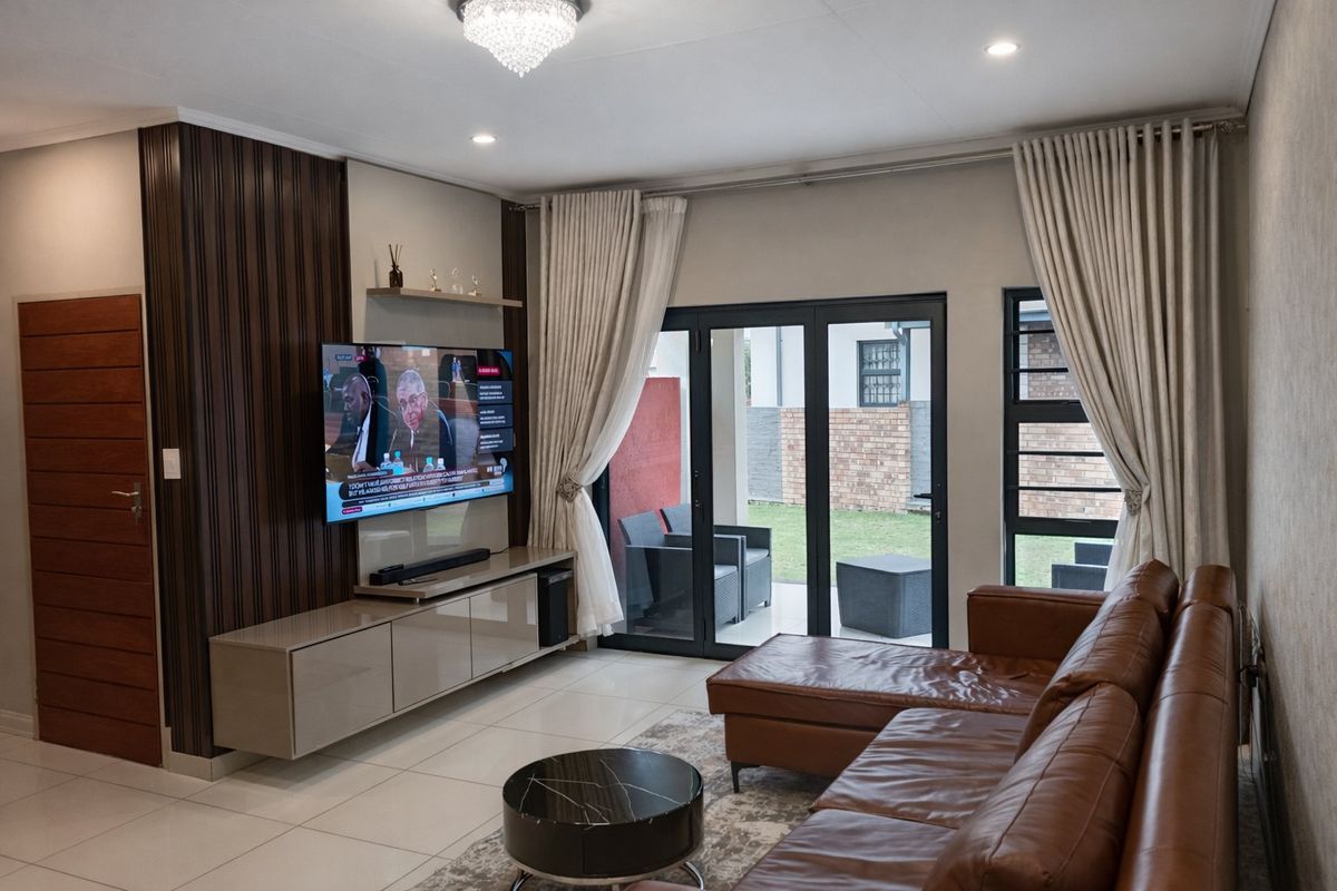 Modern living room featuring tiled floors, built-in media cabinetry, feature wall paneling, and large aluminium sliding doors providing access to the patio.