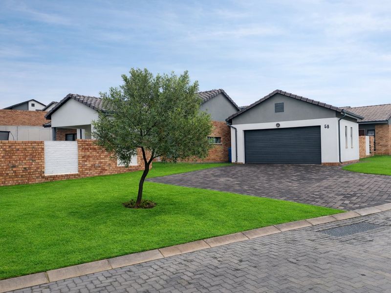 Front exterior view of a modern townhouse featuring a paved driveway, automated garage, and well-maintained lawn with a brick boundary wall.