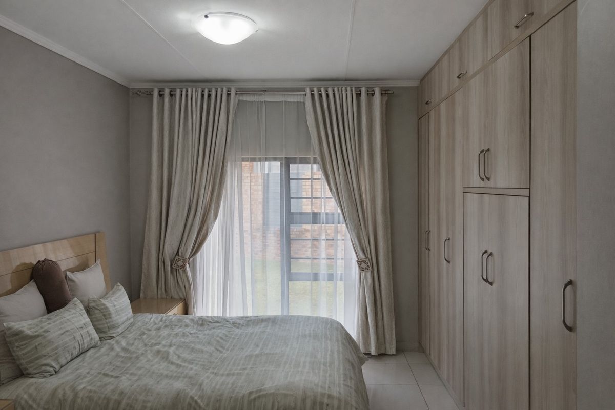 A well-maintained bedroom featuring extensive built-in cupboards, neutral tiled flooring, and a sliding door providing access to the exterior.