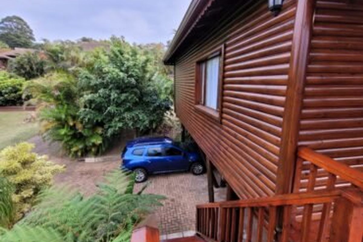 A view of the rear exterior of a timber log townhouse, featuring a raised wooden staircase and a paved driveway area below.