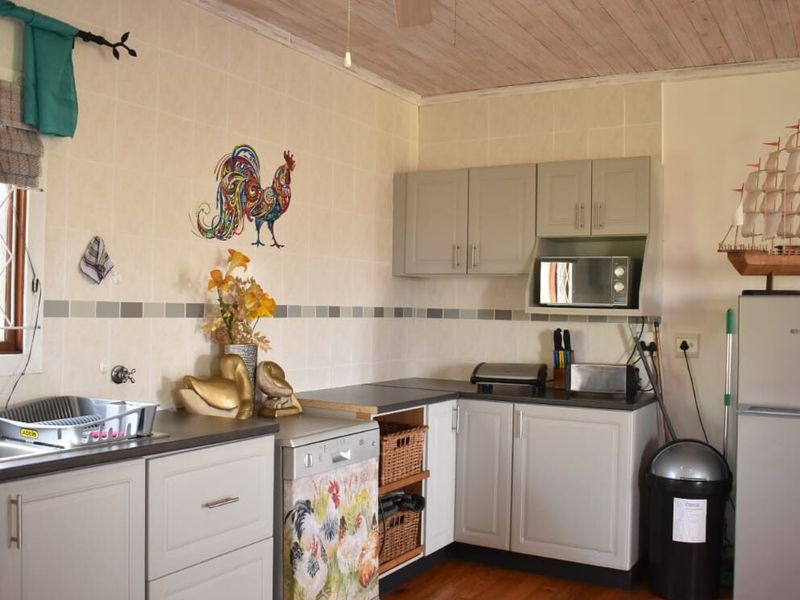 A functional kitchen featuring light grey cabinetry, timber ceiling and flooring, tiled backsplash, and a stainless steel sink.