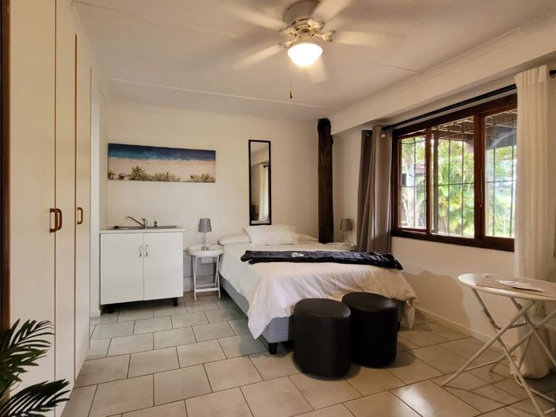A bedroom featuring tiled flooring, built-in cupboards, and a ceiling fan, with window security bars providing natural light.