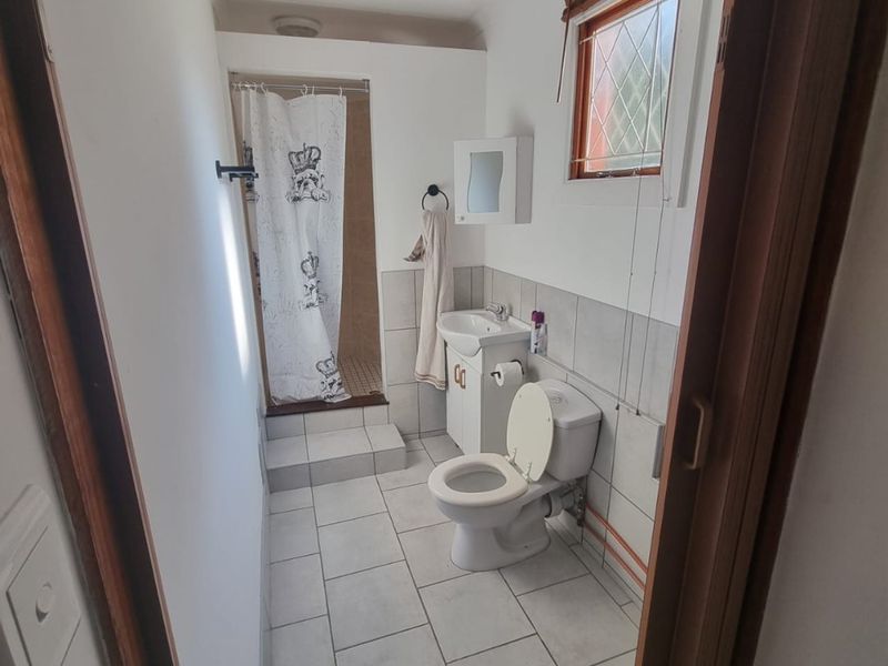 A functional bathroom featuring a shower, toilet, and vanity basin with tiled finishes and a window for natural light.