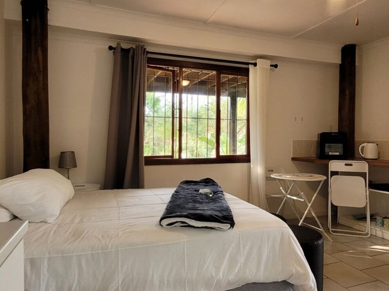 A bedroom featuring tiled flooring, wooden support pillars, and a built-in desk area with a window overlooking the exterior.
