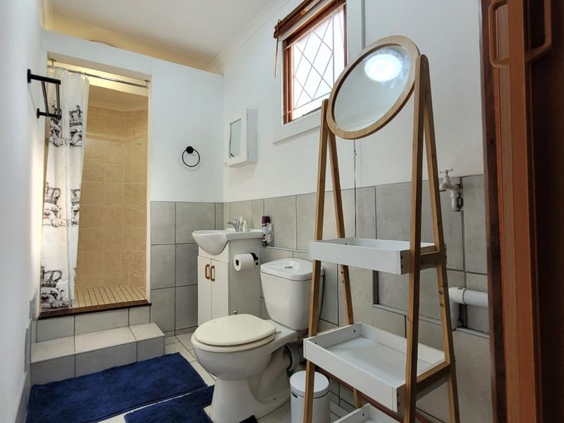 A functional bathroom featuring a shower enclosure, pedestal basin, toilet, and tiled splashback with a leaded glass window.
