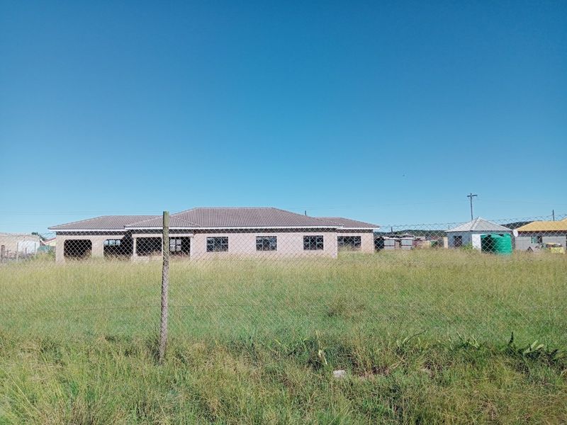 A wide-angle view of a single-story residential property under construction, featuring a tiled roof and perimeter chain link fencing on a large plot.