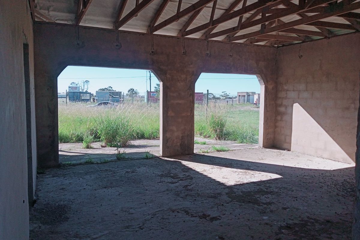 An unfinished interior space featuring exposed timber roof trusses, concrete flooring, and large arched openings leading to the exterior.