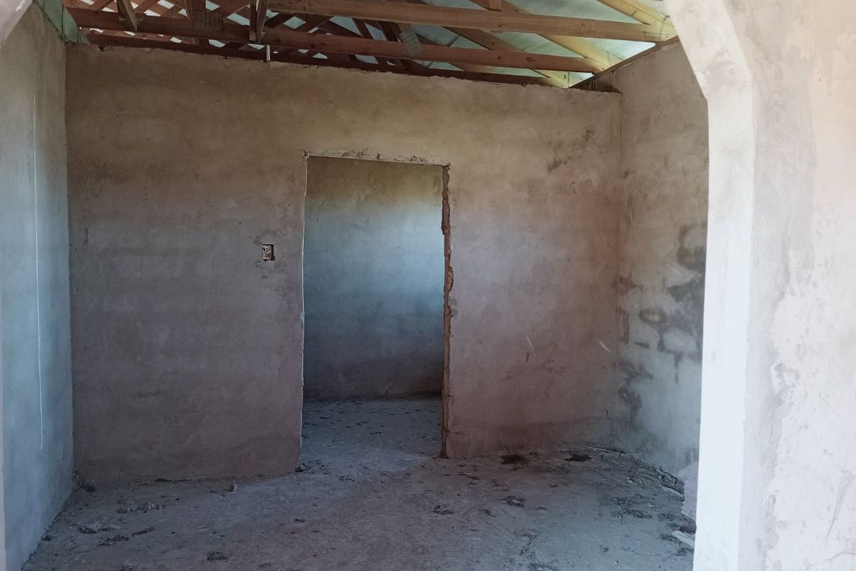An unfinished interior room featuring exposed timber roof trusses, plastered masonry walls, and an arched doorway, currently in a shell construction state.