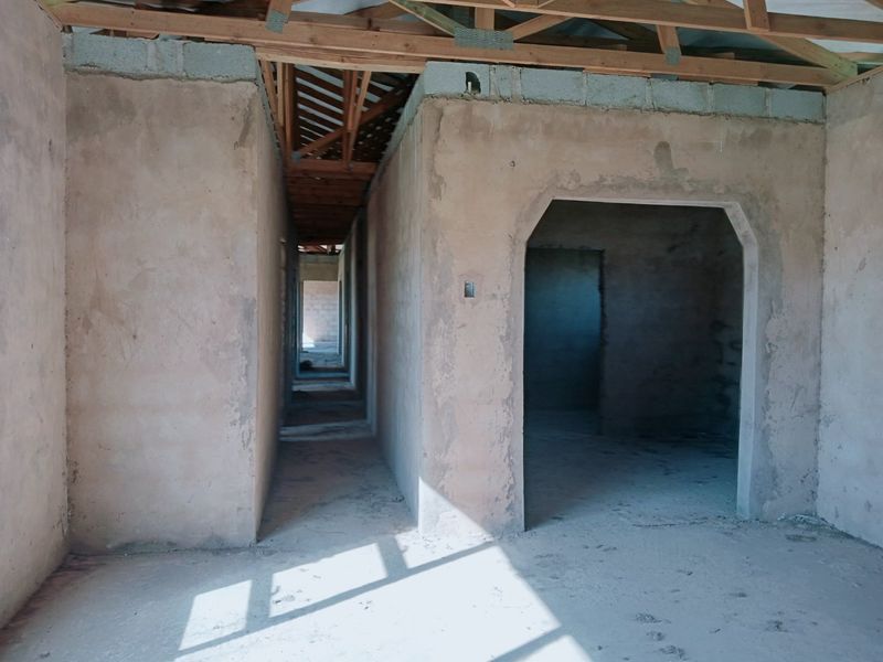 An unfinished interior hallway space showing exposed timber roof trusses, plastered masonry walls, and cement screed flooring in a construction phase.