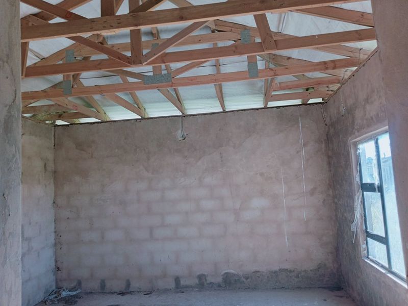 An unfinished interior space featuring exposed timber roof trusses and raw masonry walls, currently in a shell condition awaiting completion.