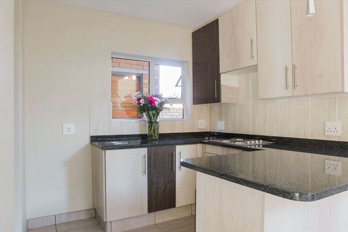 A clean, modern kitchen featuring granite countertops, light wood-tone cabinetry, a built-in gas hob, and neutral tiled flooring.