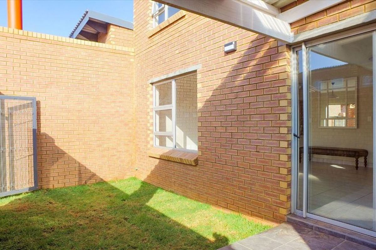A private rear courtyard featuring face brick walls, a small lawn area, and a sliding glass door providing access to the interior living space.