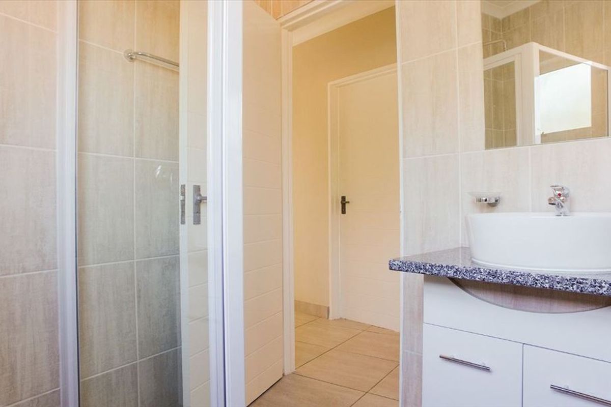 A clean and functional bathroom featuring a shower enclosure, a modern vessel sink set on a granite countertop, and neutral wall and floor tiling.