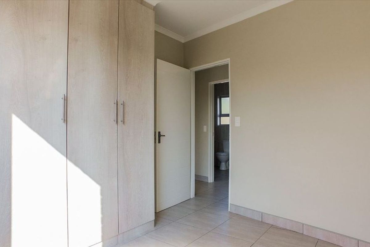 A bright, empty bedroom featuring neutral-toned tiled flooring and modern built-in cupboards, with an adjacent doorway leading to a bathroom.