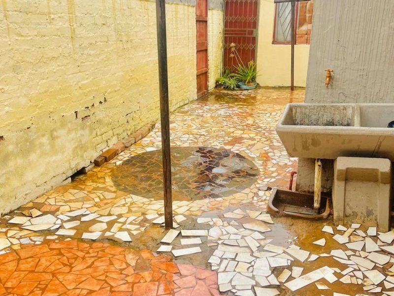 Rear courtyard area featuring a concrete wash basin, stone paving, and a boundary wall, offering potential for outdoor improvement and landscaping.