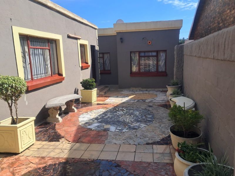 A paved rear courtyard area featuring decorative tile work, security bars on windows, and enclosed by a boundary wall.