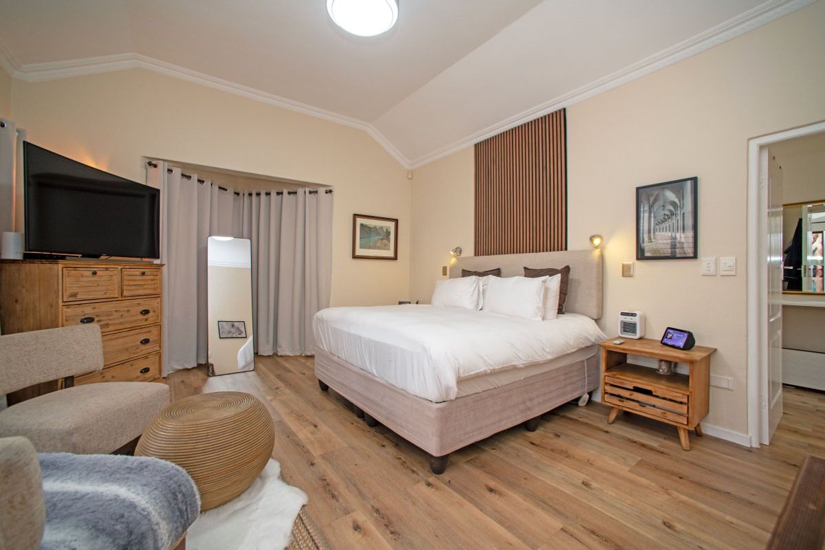 Spacious bedroom featuring vaulted ceilings, timber-look flooring, and a decorative wood-paneled feature wall behind the bed area.