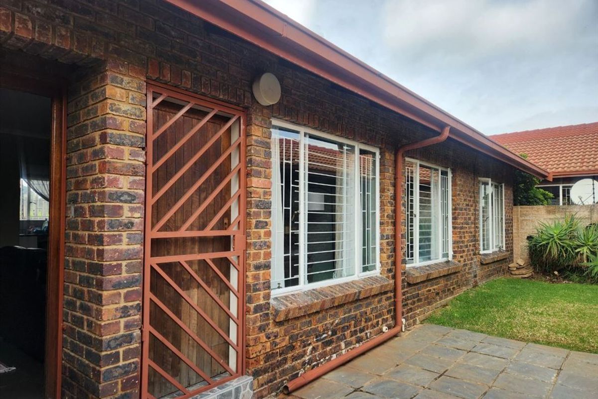 Rear exterior view of the townhouse featuring face brick construction, a paved patio area, security gates, and window security bars.