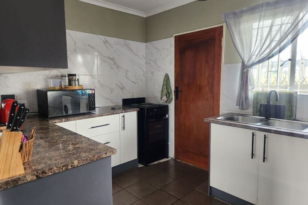 A functional kitchen featuring granite-style countertops, marble-look wall tiling, a double basin sink, and a freestanding stove with built-in cabinetry.