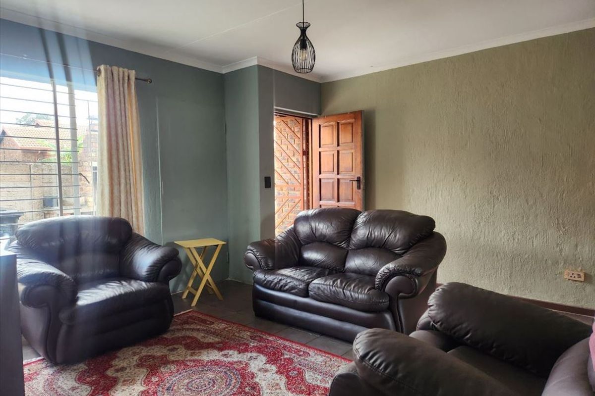 A living room featuring tiled flooring, a pendant light fixture, and a timber door leading to the exterior.