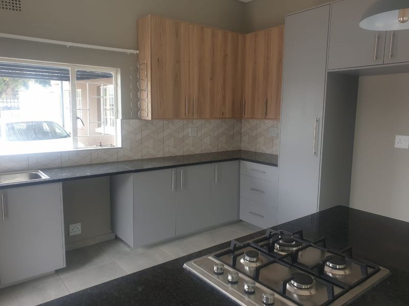 Modern kitchen featuring light grey and wood-tone cabinetry, granite countertops, a built-in gas hob, and a stylish geometric tiled backsplash.