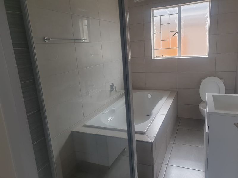 A clean, modern bathroom featuring a built-in bathtub, separate glass shower enclosure, toilet, and vanity basin with neutral wall and floor tiling.