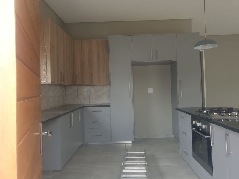 Modern kitchen featuring two-tone cabinetry, granite countertops, built-in oven, gas hob, and tiled flooring in a clean, contemporary layout.