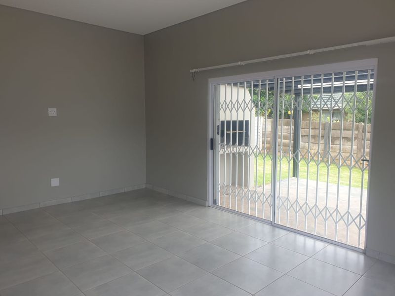 A bright, empty living area featuring neutral tiled flooring and a sliding glass door with a security gate leading to the outdoor patio.