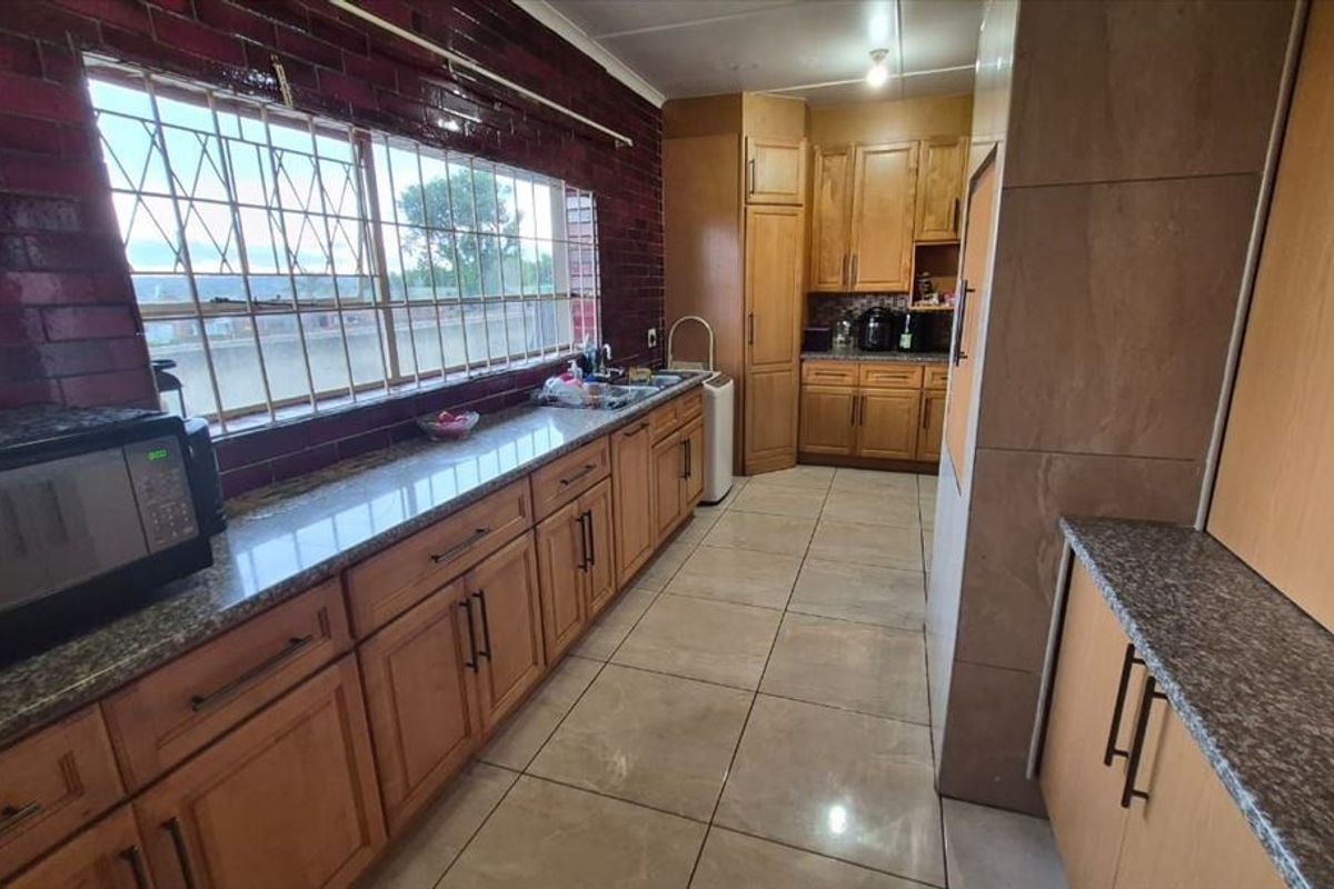 A functional kitchen featuring wooden cabinetry, granite countertops, tiled flooring, and a large window with security bars.