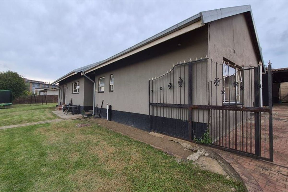 Side view of the house featuring a paved driveway, metal security gate, and a spacious lawn area.