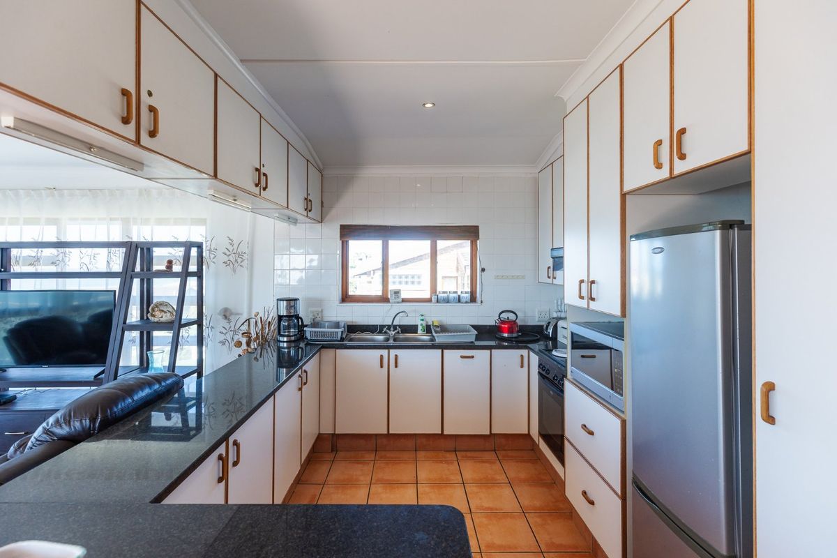 A functional kitchen featuring white cabinetry with wood trim, dark countertops, tiled backsplash, and integrated oven and hob.