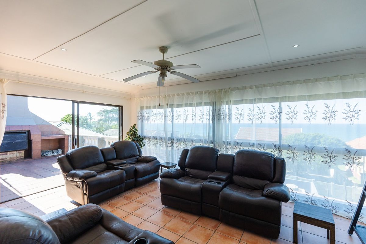 Spacious living area featuring tiled flooring, a ceiling fan, and large sliding glass doors opening onto a covered patio with ocean views.