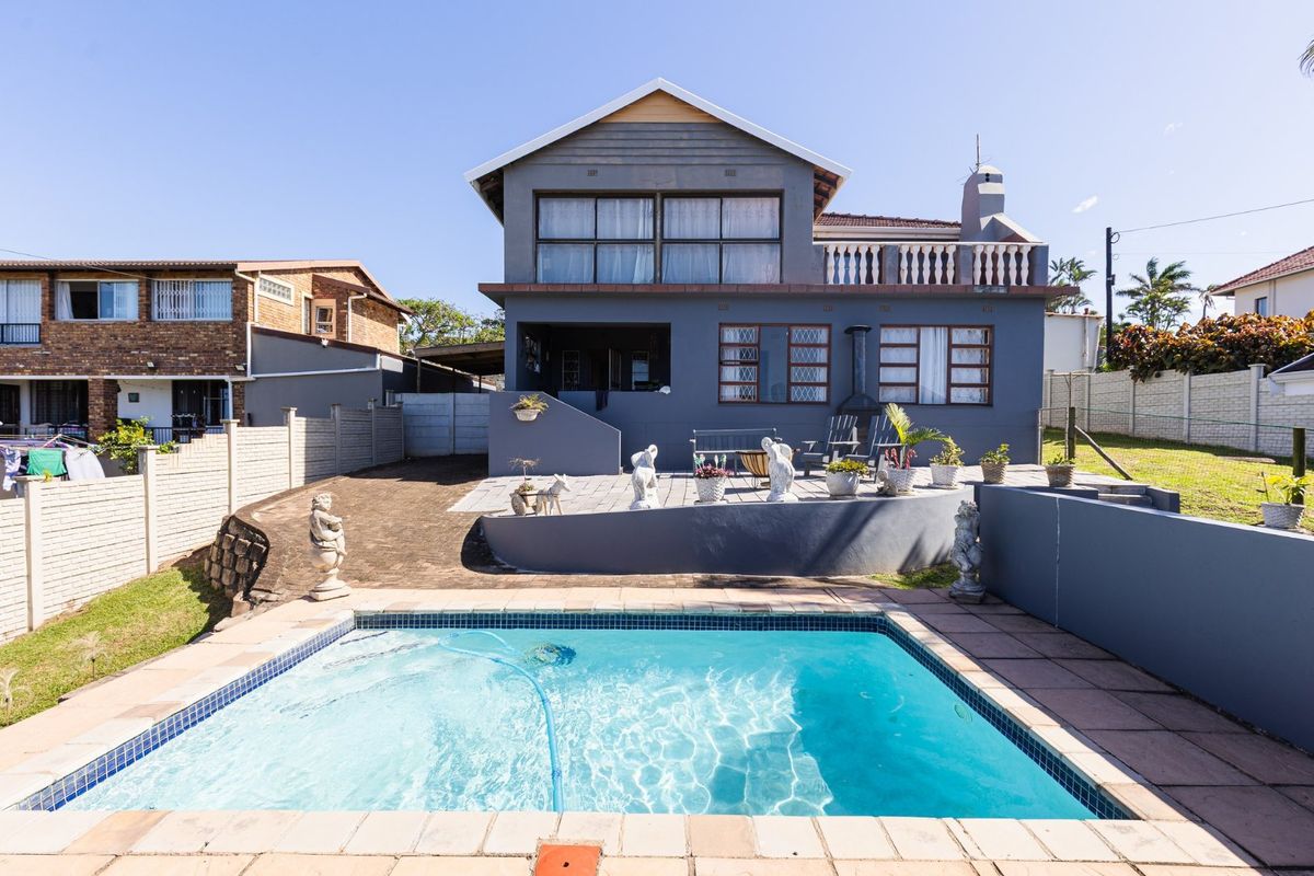 Rear view of a two-story house featuring a paved patio area, a swimming pool, and a balcony with balustrade railing.