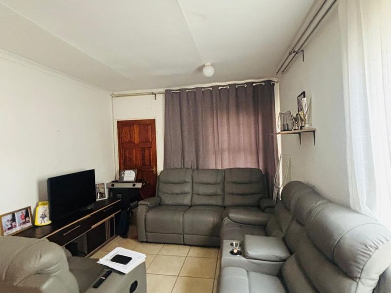 A living room featuring tiled flooring and curtain rails, showing signs of wear including visible ceiling panel damage.
