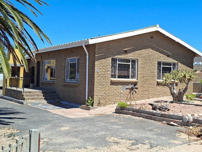 Front view of a single-story brick house featuring a metal roof, security bars on windows, and a paved driveway area.