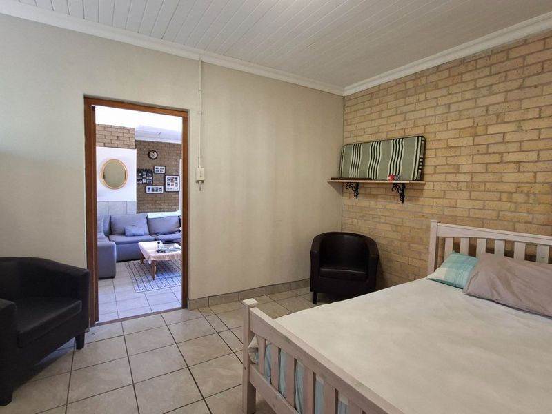A bedroom featuring exposed brick wall detailing, tiled flooring, and a tongue and groove ceiling, with an open doorway leading to an adjacent living area.