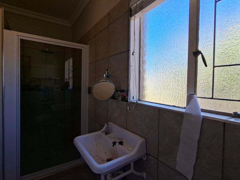 A functional bathroom featuring a shower enclosure, wall-mounted basin, and tiled walls, requiring cosmetic updates to modernize the space.