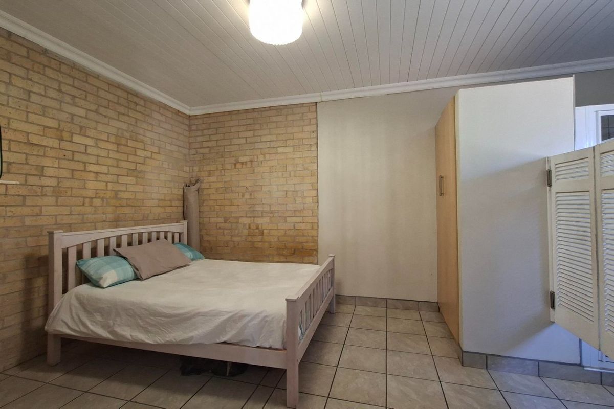 A bedroom featuring exposed brick walls, tiled flooring, and a built-in wardrobe with a tongue and groove ceiling.