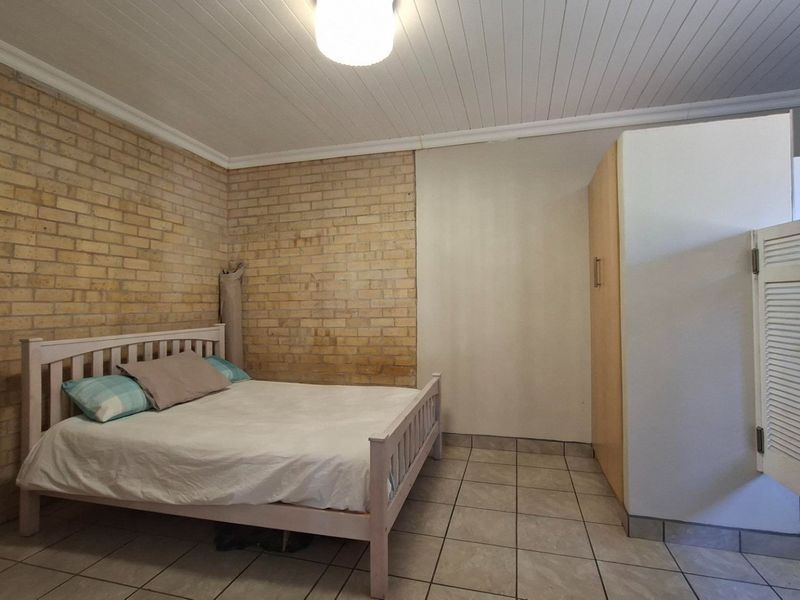 A bedroom featuring exposed brick walls, tiled flooring, and a built-in wardrobe with a tongue and groove ceiling.