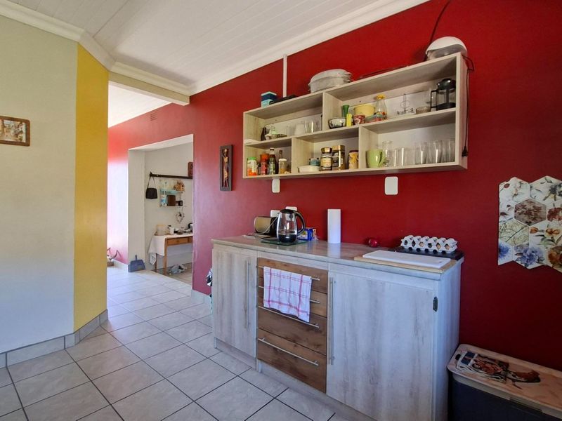 A kitchen area featuring built-in cabinetry, wall-mounted shelving, and tiled flooring, with a view leading into an adjacent utility space.