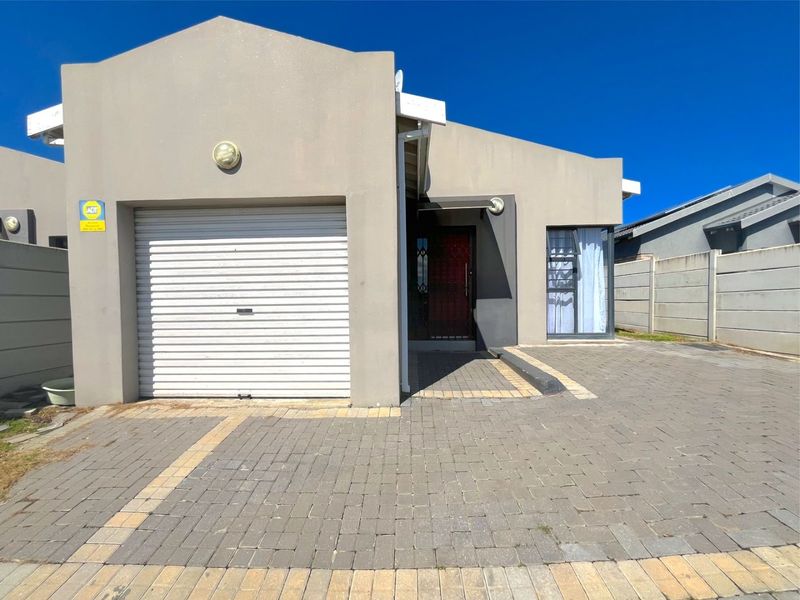 Front elevation of a modern house featuring a single roller garage door, paved driveway, and secure entrance with a security gate.