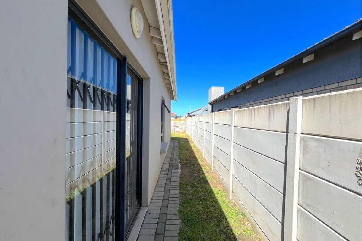 A narrow side passage featuring a paved walkway, precast concrete boundary wall, and access to the home via a sliding glass door.