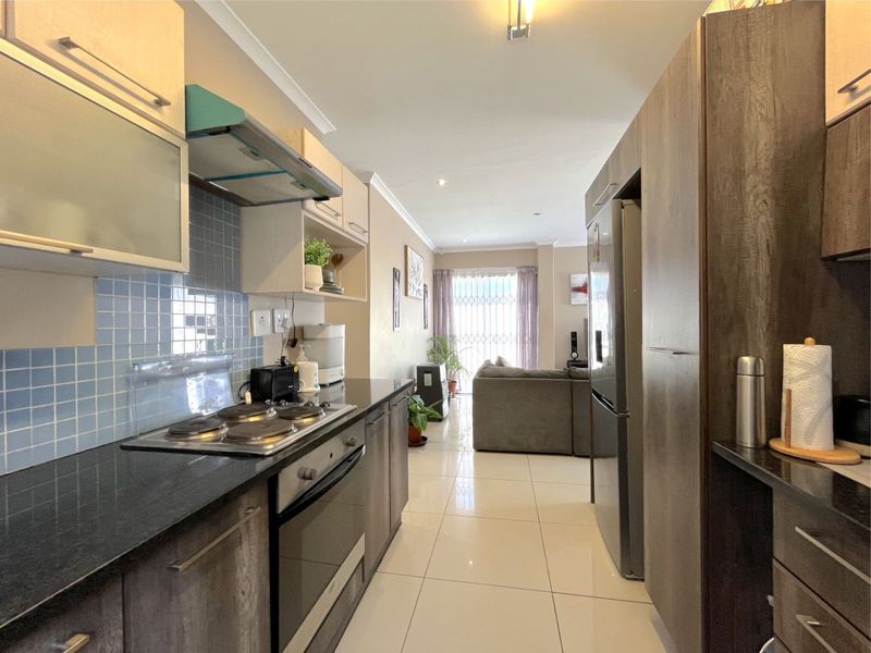 Open-plan kitchen featuring dark wood cabinetry, granite countertops, and integrated appliances, flowing seamlessly into the adjacent living area with tiled flooring throughout.
