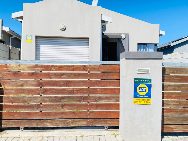 Front elevation of a modern residential property featuring a timber sliding gate, concrete boundary wall, and integrated garage.
