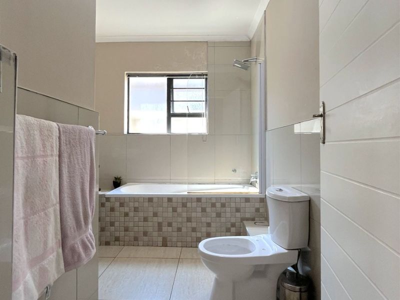 A functional bathroom featuring a built-in bathtub with a shower screen, a toilet, and neutral tiled finishes throughout.