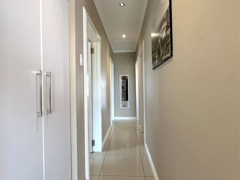 A clean and well-maintained hallway featuring neutral tiled flooring, recessed downlighting, and ample built-in storage cupboards.