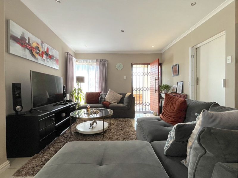 A well-maintained living room featuring tiled flooring, recessed downlighting, and direct access to the exterior through a secure timber entrance door.
