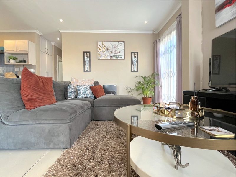 An open-plan living area featuring tiled flooring, recessed downlights, and access to an outdoor space through a security gate.